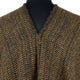 A brown tweed fabric poncho with a V-shaped neckline displayed on a black mannequin torso, emphasizing the woven texture and pattern.