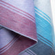 Tinizaray baby alpaca wool blanket – a soft, woven textile features a colorful pattern of intersecting stripes in blue, purple, and red tones, draped gracefully, highlighting its texture and intricate stitching