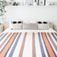 Sopoto baby alpaca wool blanket – a neatly made bed features striped bedding and decorative pillows, situated in a minimalist room with plants and a shelf displaying various art pieces and decor items
