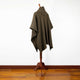 Zampu thick llama wool hooded poncho – a mannequin displays a dark plaid poncho with a high collar. It stands in a room with wooden flooring and a white wall, creating a minimalist setting