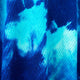 A close-up of blue and turquoise tie-dye fabric with a textured weave pattern, creating vibrant, abstract designs.