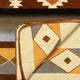 A woven textile shows geometric patterns in earthy tones. A corner is flipped, revealing diamond motifs underneath. The context suggests a Southwestern-inspired design.
