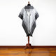 A gray and white patterned poncho with a hood drapes over a mannequin, standing on a hardwood floor against a plain white wall.