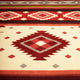 Rug with geometric patterns, featuring red and gray diamonds against a beige background, is displayed flat. The design includes horizontal stripes with varying shades and smaller diamond motifs.