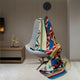 A brightly patterned blanket drapes over a gray swivel chair in a minimalist room, with a clock on the wall and decorative giraffe figurines on a wooden shelf.