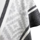 A soft, patterned fabric drapes gently, featuring grayscale geometric designs, including zigzag and stripe motifs. The material appears cozy and is set against a plain background.