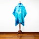 A vibrant, blue tie-dye poncho hangs on a wooden stand, set against a plain white wall and wooden floor, highlighting its textured and colorful design.