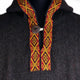 A dark, textured garment features an ornate collar with red and yellow geometric patterns. A coconut shell button fastens the front, highlighting the garment's ethnic-inspired design.