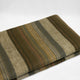 Atocha alpaca wool throw blanket – a folded, striped fabric in shades of green, brown, and gray rests on a plain white surface, showcasing soft, textured material with earthy colors