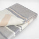 Yankuam baby alpaca wool blanket – a folded blanket displays beige, gray, and cream stripes, resting on a plain white surface, emphasizing its soft texture and subtle patterns