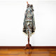 A mannequin displays a patterned poncho with geometric designs in blue, brown, and cream. It stands on a wooden stand on a brown, polished floor against a plain white background.