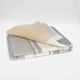 Yankuam baby alpaca wool blanket – a folded, multicolored blanket lies neatly, displaying gray, beige, and cream stripes. It rests on a plain, white surface, highlighting its soft texture and modern design