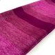 Chontamarca baby alpaca wool blanket – a folded, gradient-colored fabric featuring shades of pink and maroon lies against a white background. The texture appears soft and wool-like, with horizontal color transitions