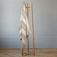 Zhumir baby alpaca wool blanket – a wooden coat rack stands upright, draped with a beige and brown striped blanket, in a room with light gray walls and a wooden parquet floor