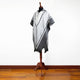 A black and white patterned poncho drapes over a wooden mannequin, displayed against a white wall on a polished wooden floor.