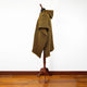 A striped poncho with a hood, displayed on a wooden mannequin stand, in a room with wooden flooring and a plain white wall background.