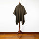 Zampu thick llama wool hooded poncho – a brown knitted poncho with a hood is draped over a wooden stand, set against a white wall and wooden floor background