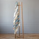 Nongora baby alpaca wool blanket – a wooden blanket rack holds a multi-colored, striped blanket. The setting is a room with light gray walls and a hardwood herringbone floor