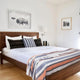 Sopoto baby alpaca wool blanket – a neatly made bed with a wooden frame features striped and patterned pillows. A striped blanket is laid on top. Two framed artworks hang on the white walls in a bright bedroom