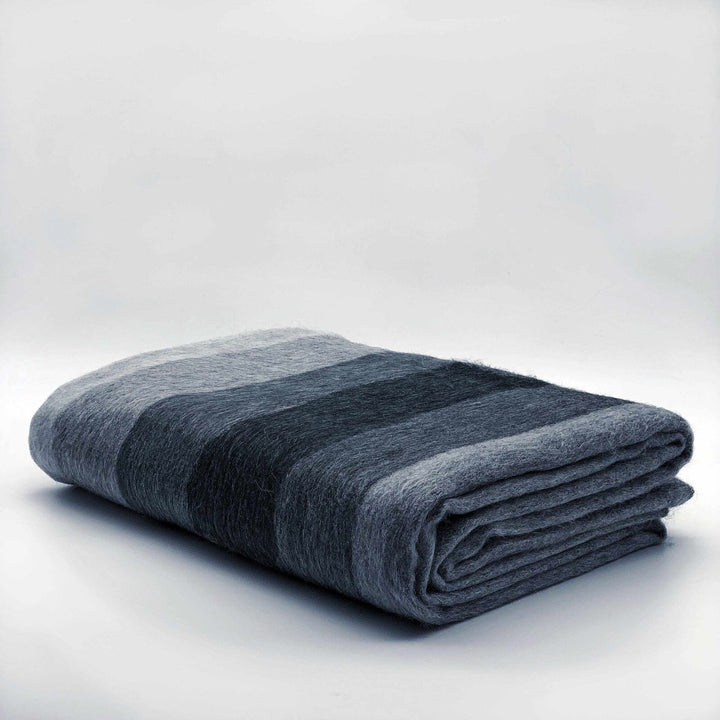 Gullian baby alpaca wool blanket – a neatly folded, striped, gray blanket lies on a light, neutral surface, emphasizing its soft texture and varying shades