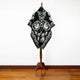 A black and white patterned poncho with geometric and floral designs is displayed on a wooden mannequin stand in a room with wooden flooring and a plain white wall.