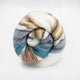 Nongora baby alpaca wool blanket – a rolled-up, multicolored striped fabric rests on a plain white background. The fabric displays shades of blue, orange, yellow, and gray in a spiral pattern