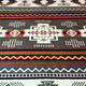 A woven rug displays intricate geometric patterns in red, green, blue, and white on a gray background, creating a vibrant and symmetrical design.