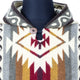 Hooded sweater features geometric patterns in shades of brown, red, and cream, secured with a wooden button. It is displayed on a black mannequin in a neutral setting.