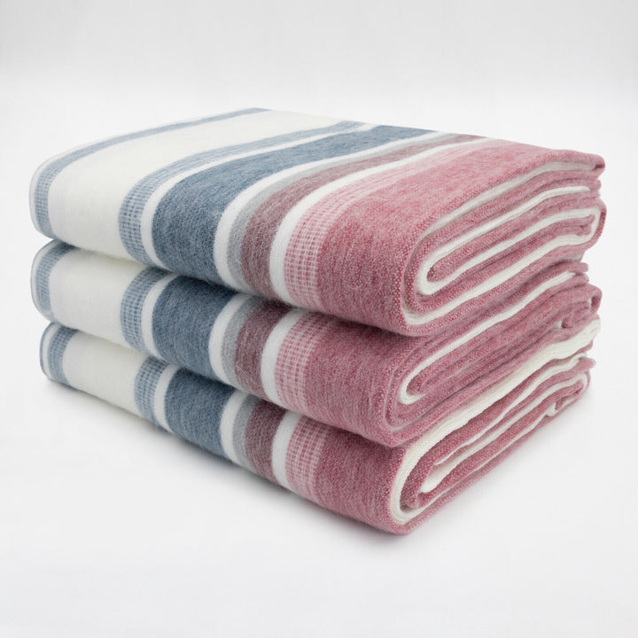 Pindo baby alpaca wool blanket – three folded blanket with pink, blue, and white stripes rest stacked on a plain white surface, suggesting neatness and organization
