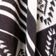 A woven fabric features bold black and white geometric patterns with stripes and angular designs. The fabric appears to be draped or folded, highlighting its texture and design.