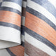 Sopoto baby alpaca wool blanket – a woven fabric is draped, featuring horizontal orange, gray, and white stripes. The texture appears soft and thick, creating a cozy look in a neutral setting
