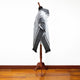 A poncho with geometric patterns drapes over a mannequin in a room with wooden flooring, set against a plain white background.