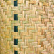 Woven basket texture featuring interlaced strips of natural and green fibers, creating a checkered pattern. The tightly woven material conveys an artisanal, handcrafted feel, filling the frame.
