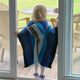 Wuachapa llama wool hooded poncho – a child in a colorful poncho stands at a glass door, looking out at wicker furniture and a grassy yard
