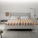 Tumbunuma baby alpaca wool blanket – a modern bed with an orange and gray striped blanket is neatly set in a minimalist bedroom. A bedside table holds a digital clock showing 10:00, a cup, and books