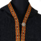 A dark garment features an intricate, colorful trim with geometric patterns around the neck, secured by a single round button. Displayed on a black mannequin in a plain setting.