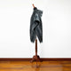 Nambija lightweight alpaca wool hooded poncho – a black and gray patterned poncho on a wooden mannequin stand, displayed in a minimalistic room with wooden flooring and a white wall background