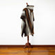 A poncho with geometric patterns and fringe edges is draped over a wooden mannequin stand against a plain white wall and hardwood floor.