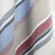 Pindo baby alpaca wool blanket – a fabric features soft diagonal stripes in blue, grey, red, and white, creating a gentle, flowing pattern. The texture appears warm and cozy, suitable for a blanket or blanket