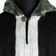 Dark and light woolen garment with a metal button fastens a hood, featuring green interior lining and a vertical opening. Displayed on a black mannequin torso against a neutral backdrop.