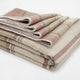 Zhumir baby alpaca wool blanket – a neatly folded stack of beige and pink striped blankets is resting on a plain white surface, showcasing their textured fabric and pattern
