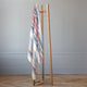 Pindo baby alpaca wool blanket – a striped blanket hangs from a wooden clothes rack, with two metal hangers visible, placed in a room with light gray walls and parquet flooring