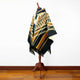 Shakai alpaca wool hooded poncho – a multicolored poncho with geometric patterns hangs on a wooden mannequin stand in a room with a wooden floor and white wall