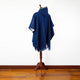 A blue poncho with a hood on a wooden stand, displayed in a room with hardwood flooring and a plain white wall.
