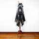 A black and gray striped poncho is draped over a wooden mannequin stand in a room with wooden floors and a white wall background.