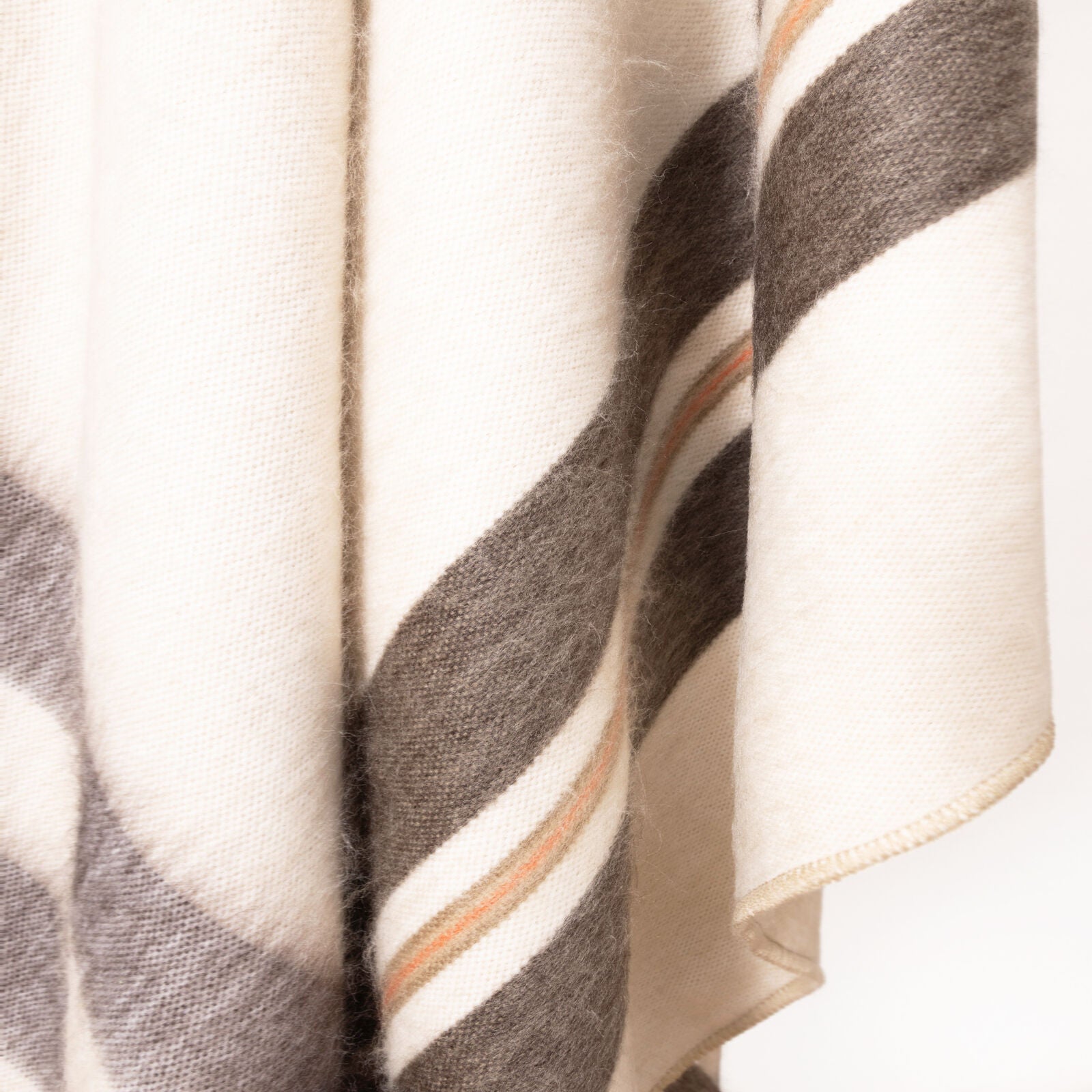 A woolen fabric hangs, featuring a pattern of wide, diagonal brown and cream stripes with thin orange accents, set against a plain background.