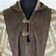 A woolen garment with brown and beige houndstooth patterns, featuring a hood and buttoned front, displayed on a black mannequin within a neutral setting.