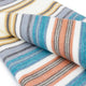 Nongora baby alpaca wool blanket – a folded fabric with horizontal stripes in blue, orange, gray, and beige lies on a white surface, showcasing its colorful pattern and soft texture