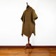 A striped poncho with a hood displayed on a wooden mannequin, standing on a polished wooden floor against a plain white wall.