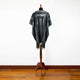 Nambija lightweight alpaca wool hooded poncho – a black and gray patterned poncho hangs on a wooden mannequin stand, centered in a room with a wooden floor and plain white wall